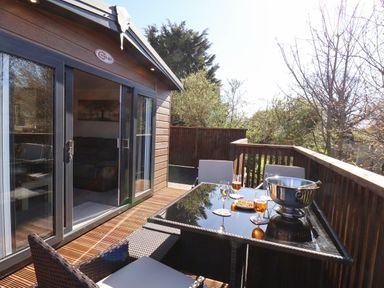 An outdoor wooden deck with a glass table and four chairs with glasses and a drink bucket at Marigold Lodge in Runswick Bay near Staithes
