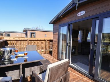 An outdoor patio with table and chairs and drinks next to a sliding glass door at Marigold Lodge in Runswick Bay near Staithes