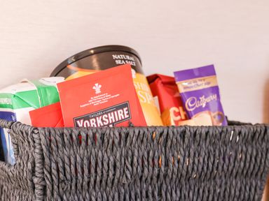 A black woven basket containing Yorkshire tea bags, a Cadbury chocolate bar, a carton of milk, and a can of sea salt crisps at Marigold Lodge in Runswick Bay near Staithes