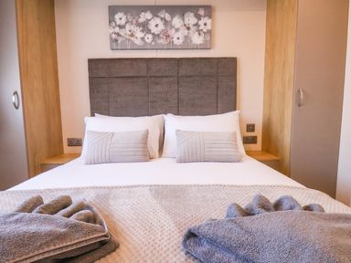 A bed with a gray headboard and white pillows between two wooden wardrobes at Marigold Lodge in Runswick Bay near Staithes
