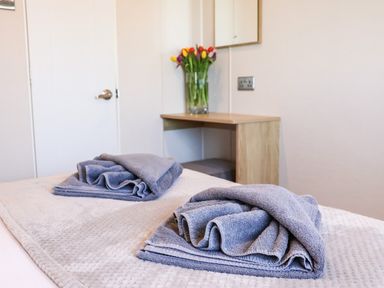 A bedroom with folded towels on a bed and a desk with a vase of tulips at Marigold Lodge in Runswick Bay near Staithes