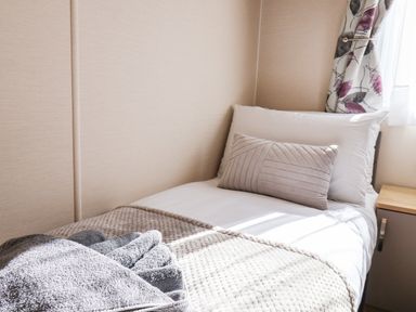 A single bed with white and beige pillows and a folded gray towel on a beige blanket at Marigold Lodge in Runswick Bay near Staithes