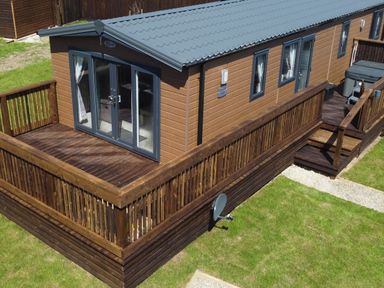 A wooden cabin with a deck and railings surrounded by grass at Marigold Lodge in Runswick Bay near Staithes