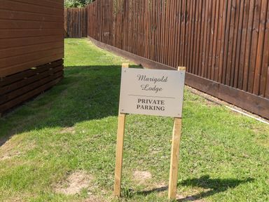 A private parking sign on grass between a wooden building and a wooden fence at Marigold Lodge in Runswick Bay near Staithes