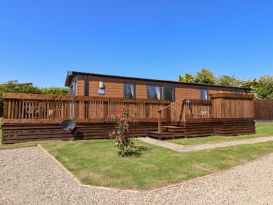 A wooden lodge with a raised deck and steps surrounded by grass and gravel paths at Marigold Lodge in Runswick Bay near Staithes