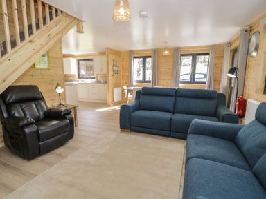 A living room with blue sofas black recliner wooden staircase and kitchen area at Sunset Lodge 5 in Llanbedr