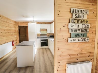 A kitchen with white cabinets a gray countertop and a wooden wall with a decorative sign at Sunset Lodge 5 in Llanbedr