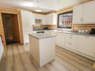 A kitchen with white cabinets a gray countertop an island wooden walls and a window at Sunset Lodge 5 in Llanbedr