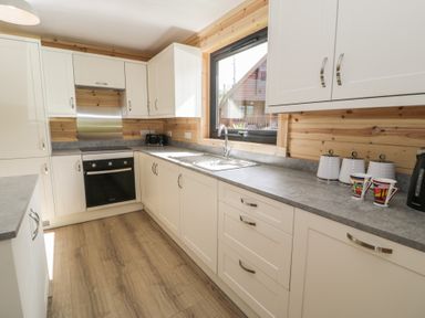 A kitchen with white cabinets gray countertops a stove a sink a window and wooden floor at Sunset Lodge 5 in Llanbedr