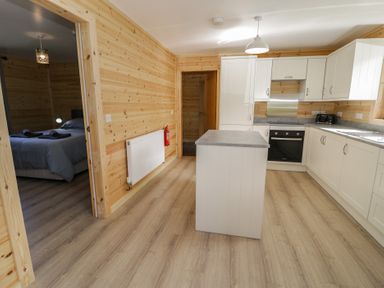 A kitchen with white cabinets an island and wooden walls next to a bedroom at Sunset Lodge 5 in Llanbedr