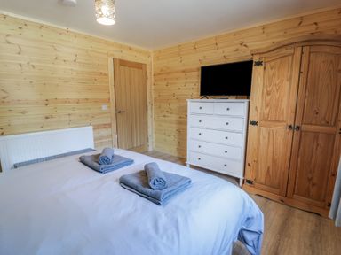 A bedroom with two beds with folded towels on top a white chest of drawers with a TV and a wooden wardrobe at Sunset Lodge 5 in Llanbedr