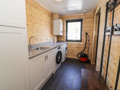 A laundry room with a sink washing machine dryer vacuum and coat hooks at Sunset Lodge 5 in Llanbedr