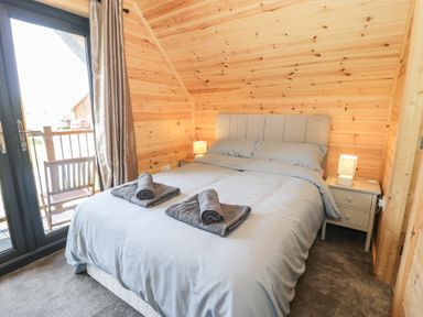 A bedroom with a double bed bedside tables and lamps next to a glass door leading to a balcony at Sunset Lodge 5 in Llanbedr