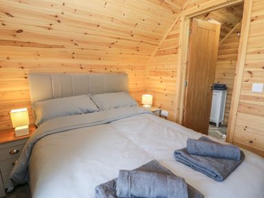 A bedroom with a bed grey bedding wooden walls lamps and folded towels on the bed at Sunset Lodge 5 in Llanbedr