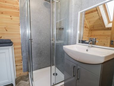 A bathroom with a glass shower enclosure a white sink with a grey cabinet a mirror and folded towels on a white cabinet at Sunset Lodge 5 in Llanbedr