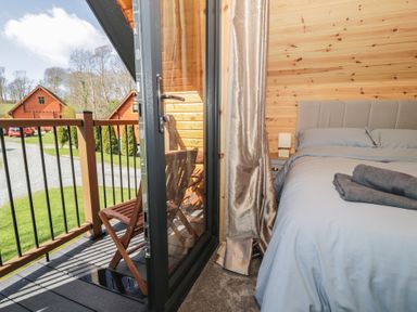 A bedroom with a bed and folded towels next to a balcony with wooden chairs at Sunset Lodge 5 in Llanbedr