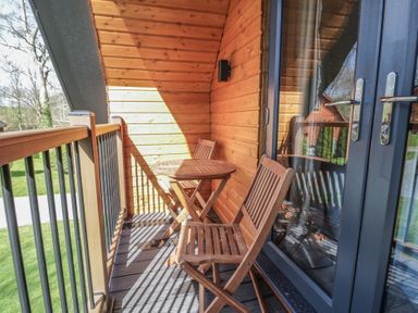 A wooden balcony with a small round table and two wooden chairs at Sunset Lodge 5 in Llanbedr