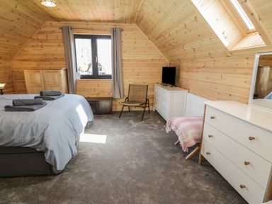 A bedroom with a bed towels dresser chair window and skylight at Sunset Lodge 5 in Llanbedr