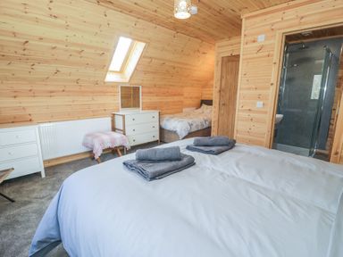 A bedroom with two beds a dresser a stool and an en suite shower at Sunset Lodge 5 in Llanbedr