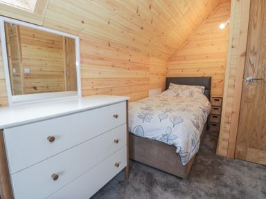 A small bedroom with a single bed a white dresser with a mirror and wooden walls at Sunset Lodge 5 in Llanbedr