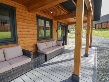 A porch area with outdoor wicker sofas and cushions at Sunset Lodge 5 in Llanbedr