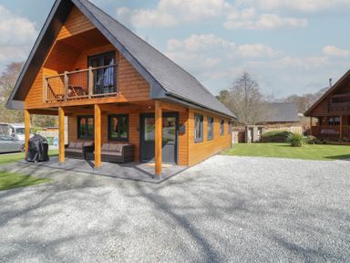A wooden lodge with a balcony and outdoor seating on a gravel driveway at Sunset Lodge 5 in Llanbedr
