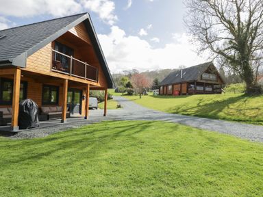 Two wooden lodges with balconies on a grassy area with a gravel driveway at Sunset Lodge 5 in Llanbedr