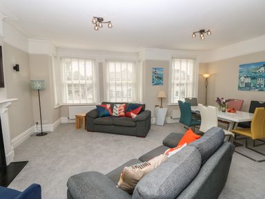 A living room with grey sofas colourful cushions a dining table with assorted chairs and paintings on the wall at Chine Heights in Bournemouth