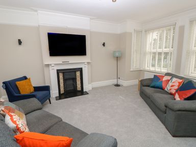 A living room with a wall mounted television above a fireplace two sofas and a blue armchair with cushions at Chine Heights in Bournemouth