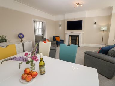 A living room with a white table holding flowers apples and a wine bottle and colorful chairs at Chine Heights in Bournemouth