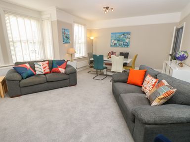 A living room with two grey sofas with colorful cushions and a dining table with multicolored chairs at Chine Heights in Bournemouth