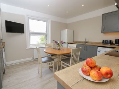 A kitchen with a round dining table and chairs a plate of apples on the counter and a window at Chine Heights in Bournemouth