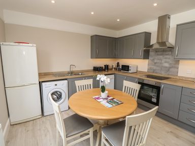 A kitchen with grey cabinets a round wooden table and white chairs at Chine Heights in Bournemouth