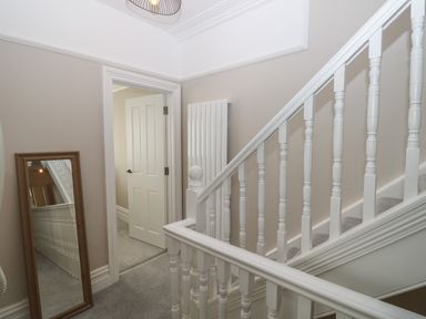 A stairway with white wooden balusters next to an open door and a full-length mirror leaning against the wall at Chine Heights in Bournemouth