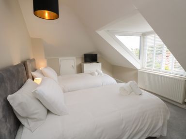 A bedroom with two beds a window with blinds and a small TV on a white chest of drawers at Chine Heights in Bournemouth