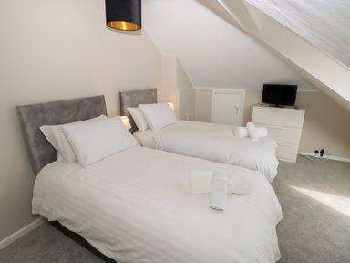 A bedroom with two single beds with white bedding and towels a chest of drawers with a TV on top at Chine Heights in Bournemouth
