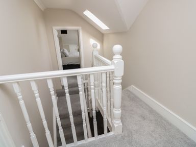 A carpeted staircase with white wooden railings leading to an upstairs hallway and a bedroom at Chine Heights in Bournemouth