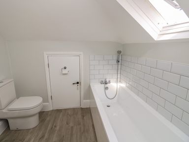 A bathroom with a toilet a bathtub with showerhead and a small door under a slanted ceiling at Chine Heights in Bournemouth