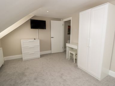 A bedroom with a TV mounted above a chest of drawers a wardrobe a desk with a chair and an open door at Chine Heights in Bournemouth
