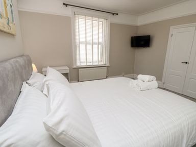 A bedroom with a double bed white linens rolled towels a nightstand window with blinds wall-mounted television and a closed door at Chine Heights in Bournemouth