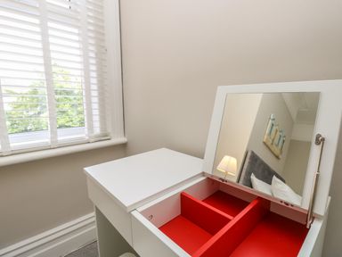 A dressing table with an open mirror and red compartments near a window with white blinds at Chine Heights in Bournemouth