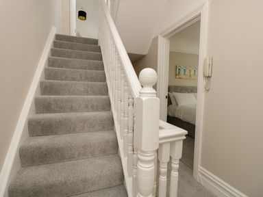 A carpeted staircase with white wooden railing next to a doorway leading to a bedroom with a bed and wall art at Chine Heights in Bournemouth