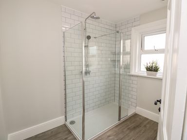 A shower enclosure with glass walls and chrome fixtures in a bathroom with tiled walls and a window with a plant on the sill at Chine Heights in Bournemouth
