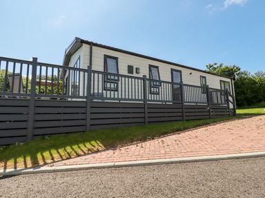 An exterior view of a single-story modular home with a fenced deck and a paved driveway at 63 The Maples in Hewas Water near Sticker