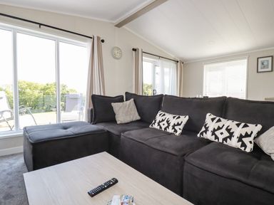 A living room with a large dark sectional sofa and cushions beside sliding glass doors at 63 The Maples in Hewas Water near Sticker
