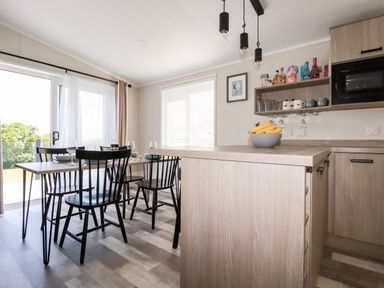 A kitchen dining area with a wooden table set with plates and glasses and black chairs at 63 The Maples in Hewas Water near Sticker