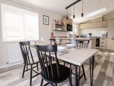 A dining table with four black chairs set with plates and glasses next to a kitchen with wooden cabinets at 63 The Maples in Hewas Water near Sticker