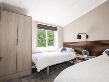 A bedroom with two beds a wardrobe a nightstand with a flower pot and a window at 63 The Maples in Hewas Water near Sticker
