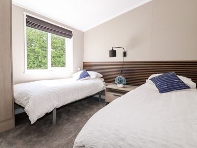 A bedroom with two single beds a nightstand with a flower pot and a window at 63 The Maples in Hewas Water near Sticker
