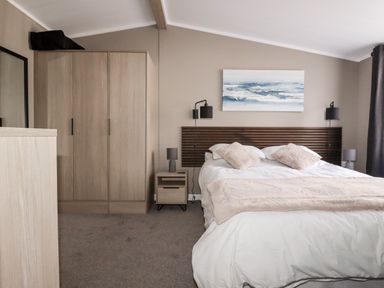 A bedroom with a bed and wooden headboard two nightstands with lamps a wardrobe a chest of drawers and a painting above the bed at 63 The Maples in Hewas Water near Sticker
